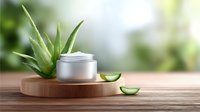 Fresh aloe vera plant with sliced leaves next to silver cosmetic cream jar on wooden platform against soft blurred green background for natural skincare products.