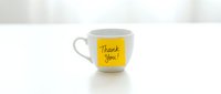 White ceramic mug with a yellow sticky note saying Thank You on a clean white surface, conveying gratitude and appreciation in a minimal style.