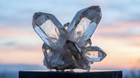 Clear quartz crystal cluster with multiple points against soft pastel sky background for healing meditation and spiritual wellness practices.
