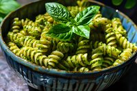 Delicious homemade pesto pasta fusilli with fresh basil leaves in rustic ceramic bowl, ready to serve for lunch or dinner meal preparation.