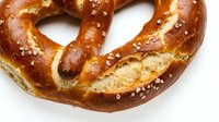 Freshly baked soft pretzel with coarse salt crystals on white background, ready for bakery, food service, or culinary design projects.