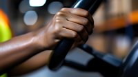 African American hand gripping black exercise equipment handle during workout at gym with blurred bokeh background lights. Close up fitness training detail.