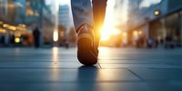 Close-up of person walking on urban pavement at sunset with dramatic lens flare and bokeh lights, low angle view showing business shoes and suit pants.