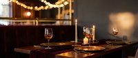 Elegant restaurant table setting with wine glasses and warm ambient lighting from string lights creating romantic dining atmosphere for special occasions.