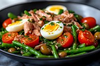 Fresh tuna salad with green beans, cherry tomatoes, boiled eggs, olives and herbs served on black plate, close up view of healthy Mediterranean meal.