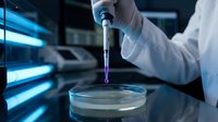 Scientist in white lab coat pipetting purple liquid into petri dish in modern laboratory with blue lighting and equipment.