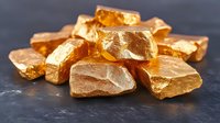 Pure gold nuggets and pieces scattered on dark stone surface, raw precious metal minerals displaying natural texture and warm metallic luster in studio lighting.