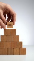 Hand placing wooden block with TRUST text on pyramid of cubes representing business foundation, reliability and confidence building concepts.