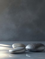 Smooth zen stones arranged on reflective surface against textured dark wall with soft natural lighting for spa wellness meditation concepts.