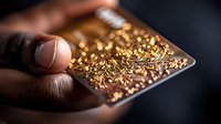Macro shot of fingers holding playing card decorated with intricate golden ornamental pattern against dark background, selective focus on luxurious details.
