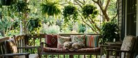 Cozy outdoor patio with wicker furniture, colorful cushions and lush hanging plants creating peaceful garden retreat for relaxation and entertaining.