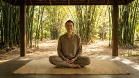 Young Asian woman practicing meditation in peaceful bamboo forest pavilion, sitting cross-legged on wooden platform in natural zen environment for mindfulness and wellness.