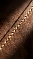 Close-up macro shot of brown leather surface with detailed stitching seam showing craftsmanship and texture for luxury goods and fashion accessories.