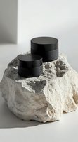 Black cosmetic jars placed on rough limestone rock against white background. Minimal product photography showcasing luxury skincare packaging design.