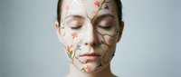 Young woman with closed eyes and delicate floral face paint featuring botanical elements for beauty and artistic makeup concepts.