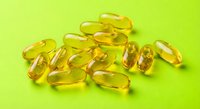 Golden yellow omega-3 fish oil capsules scattered on bright green background for health and wellness supplement advertising and medical content.