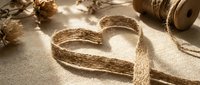 Heart-shaped burlap ribbon with natural jute twine and pine cones on rustic fabric background for craft projects and romantic decorations.