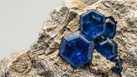 Blue sapphire gemstone crystals embedded in natural rock matrix showing hexagonal crystal structure and brilliant color saturation for jewelry design.