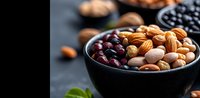 Fresh mixed nuts and berries in black ceramic bowl on dark background, healthy protein snack with almonds, pistachios and cranberries, selective focus.