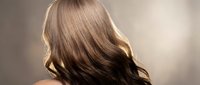 Woman with long flowing brown hair showcasing healthy shine and movement against soft neutral background for beauty and haircare concepts.