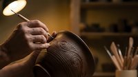 Skilled artisan hands carving intricate decorative patterns into wooden bowl in warm workshop lighting with traditional woodworking tools visible in background.