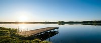 Wooden dock extending into calm lake at sunrise with clear blue sky and distant treeline, suitable for travel, nature, and outdoor recreation concepts.