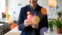 Smiling businessman holding glowing light bulb with colorful bokeh effects in modern office workspace representing innovation and creative ideas.