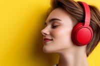 Young Caucasian woman with short brown hair and closed eyes enjoying music through red wireless headphones against vibrant yellow background.