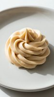 Piped swirl of creamy caramel buttercream frosting on white ceramic plate, ready for cake decorating, baking, and confectionery design projects.