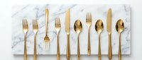 Flat lay arrangement of golden cutlery set on marble surface, featuring forks, knives and spoons for dining and table setting design projects.