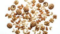 Mixed nuts collection with walnuts, almonds, cashews and various healthy snacks scattered on white background for cooking and nutrition concepts.