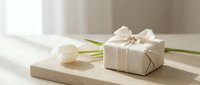 Elegant gift box wrapped in natural linen fabric with white tulip flower on wooden surface, minimalist present for special occasions and celebrations.