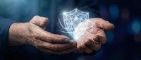 Businessman hands protecting glowing digital shield icon representing cybersecurity, data protection and network safety in modern technology environment.