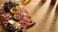 Gourmet charcuterie board with cured meats, artisan cheeses, grapes, nuts and honey on rustic wooden table for entertaining and wine pairing occasions.