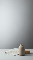 Minimalist still life composition with beige ceramic vase, linen fabric and wooden block on white surface against gradient gray wall for modern interior design.