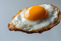 Close-up of sunny side up fried egg with crispy brown edges and bright orange yolk on light background, showcasing texture and detail in food photography.