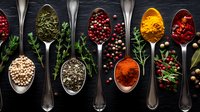 Aromatic spices and herbs in vintage silver spoons on dark background, colorful seasoning mix of peppercorns, turmeric, paprika, dried herbs and berries.