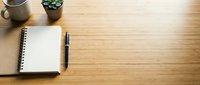 Minimalist wooden desk workspace with open notebook, pen, coffee mug and small plant. Clean office setup with natural wood grain texture and copy space for productivity.