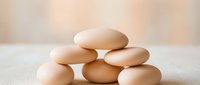 Fresh brown eggs stacked in pyramid formation on white surface with soft natural lighting for cooking and nutrition concepts.