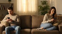 Young couple sitting apart on couch using smartphones, relationship problems, communication issues, social media addiction in modern living room.