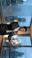 Young Asian businessman using holographic interface technology in modern office with city skyline view for futuristic business presentations.