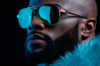 Close up portrait of African American man with beard wearing reflective sunglasses and fur collar in dramatic blue lighting creating modern urban mood.