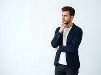 Young Caucasian man in navy blazer and white shirt standing in thoughtful pose with hand to chin against white background for business and professional concepts.
