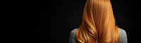 Back view of woman with long, flowing copper-colored hair against dark background, showcasing healthy, shiny locks for beauty and haircare advertising.