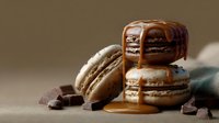 Chocolate macarons with caramel drizzle and dark chocolate pieces on neutral background for dessert menu, bakery advertising, food blog content.