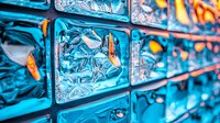 Decorative glass blocks wall with turquoise blue illumination and orange accents creating modern architectural detail, abstract geometric pattern.