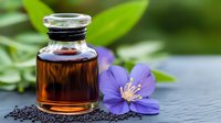 Small glass bottle with brown essential oil and fresh purple wildflower on dark stone background with green leaves, natural aromatherapy concept.