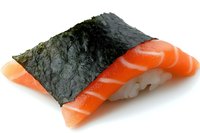 Fresh salmon nigiri sushi piece wrapped with nori seaweed strip on white background, traditional Japanese cuisine preparation showing vibrant orange fish texture.