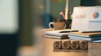 Professional workspace with wooden blocks displaying 2027 year numbers on desk with laptop, notebooks, and coffee cup for business planning and goal setting.