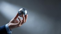 Close-up of businessman hand holding geometric crystal cube against gray background, representing innovation, technology, and strategic business solutions.